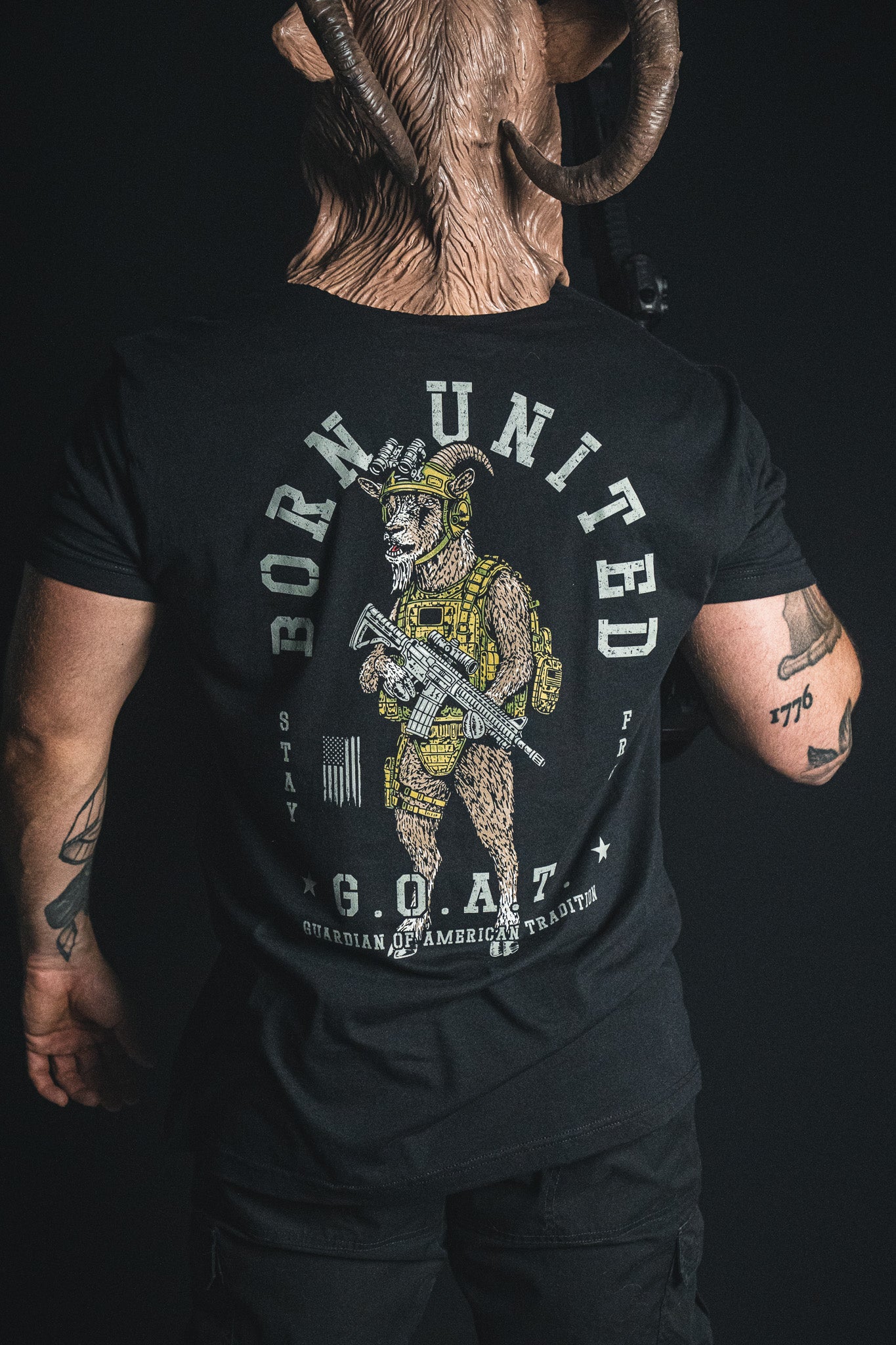 A person wearing the Born United Private Label “G.O.A.T.” shirt, which features an armed goat in tactical gear alongside the phrases “Born United” and “G.O.A.T. Guardian of American Tradition,” making this statement tee a bold celebration of American tradition.