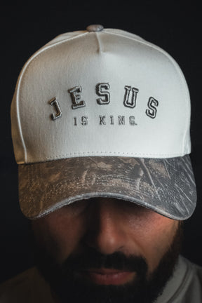 A person wearing the Born United Private Label “Jesus is King - Ivory and Deadwood Camo Snapback” is photographed against a dark background.