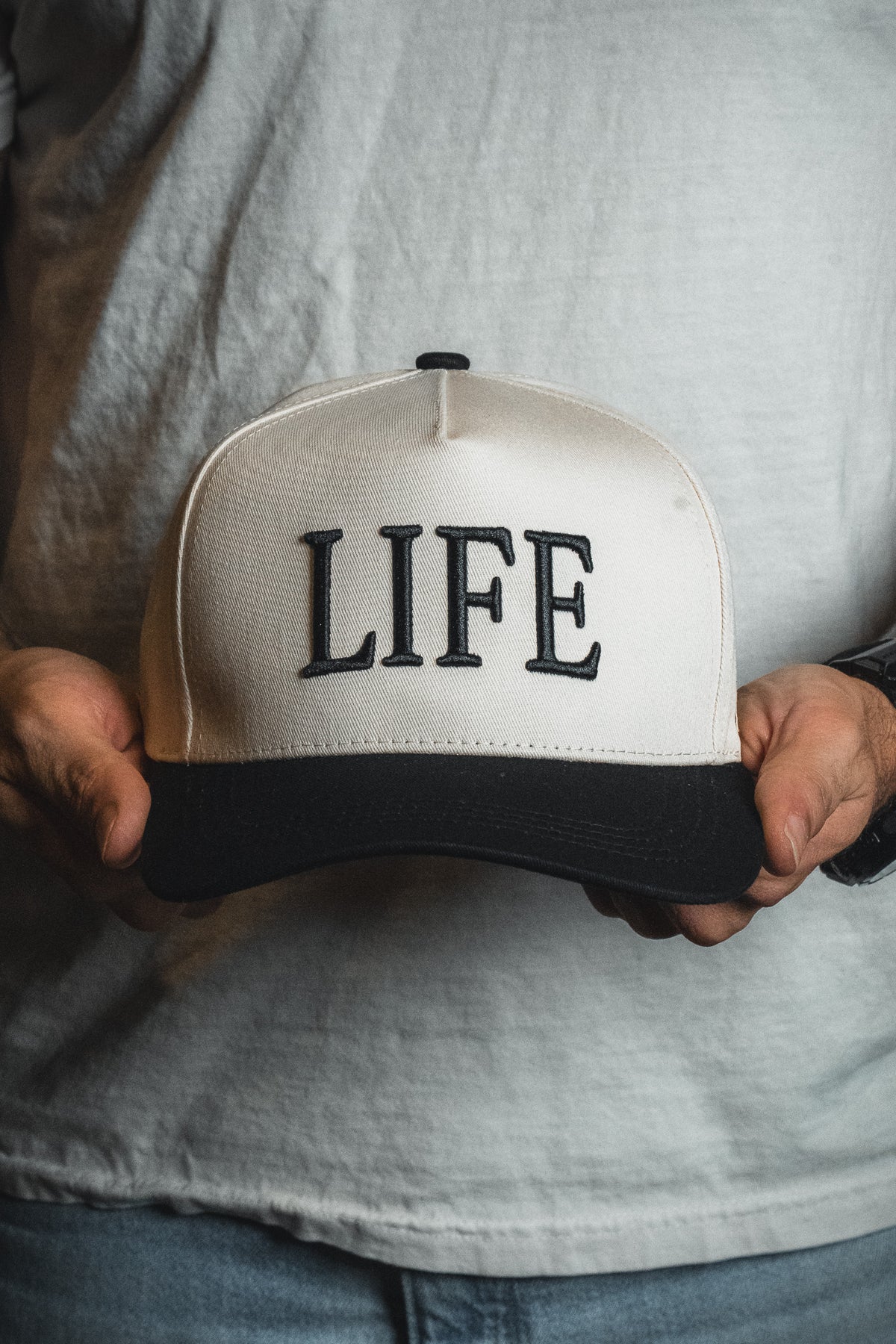 A person holding the LIFE - Ivory and Black Snapback by Born United Private Label, featuring the word “LIFE” embroidered on the front—a cap that showcases a spiritual message.