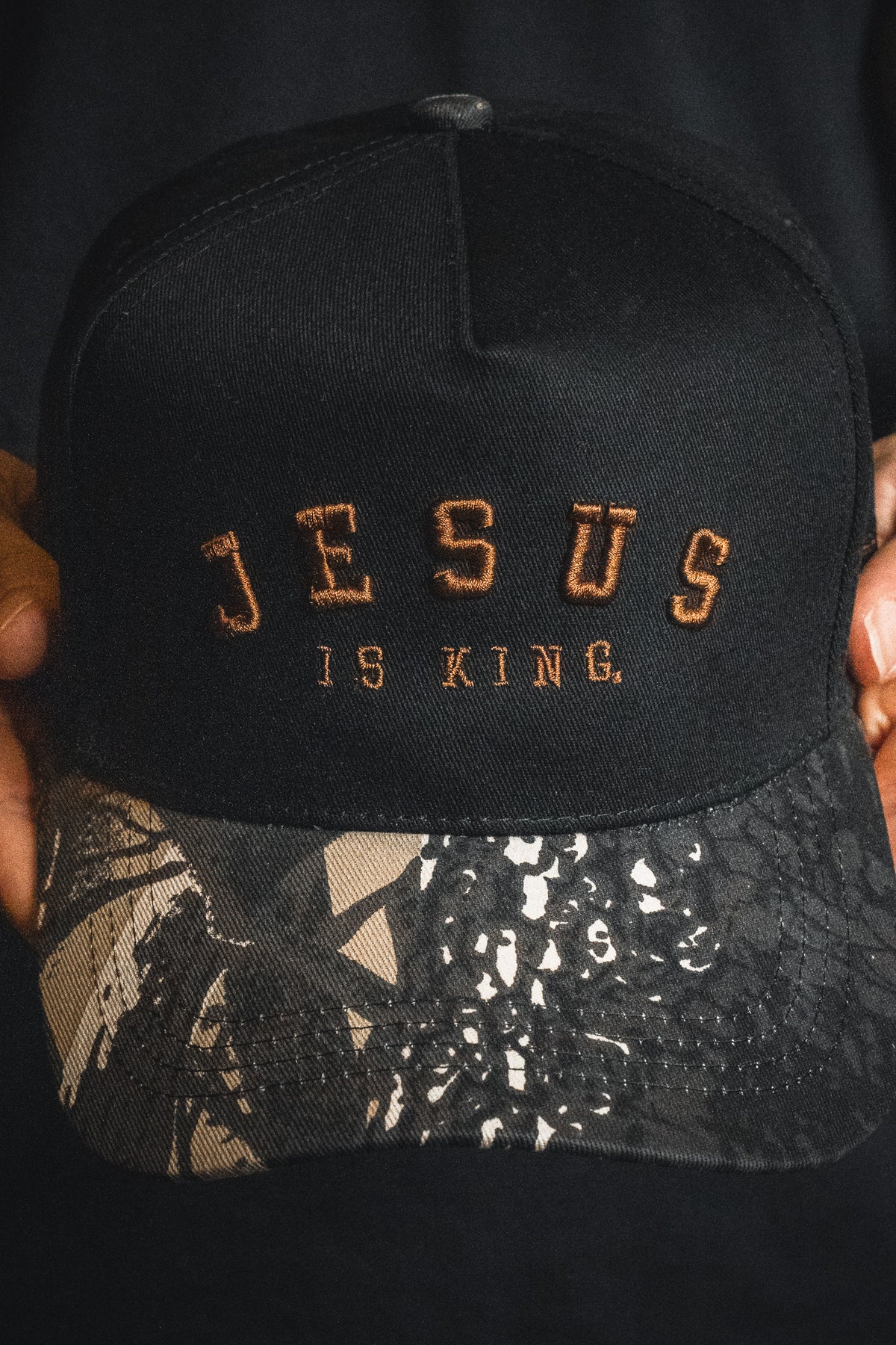 Introducing the Jesus is King - Black and Darkwood Camo Snapback by Born United Private Label. This black snapback hat features striking brown embroidery with the text “JESUS IS KING.” Highlighting its unique style, the brim displays an eye-catching black, white, and gray abstract camo pattern.