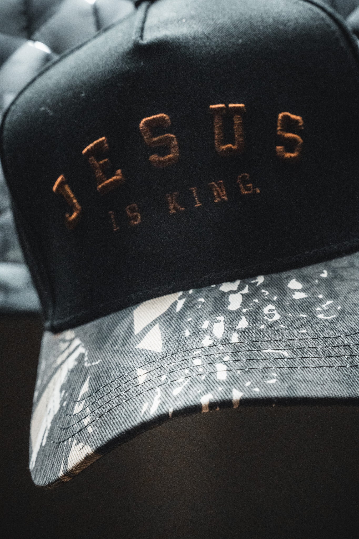 The Born United Private Label “Jesus is King - Black and Darkwood Camo Snapback” features “JESUS IS KING.” embroidered in gold on the front, with a brim displaying a black, white, and gray abstract Darkwood camo pattern.