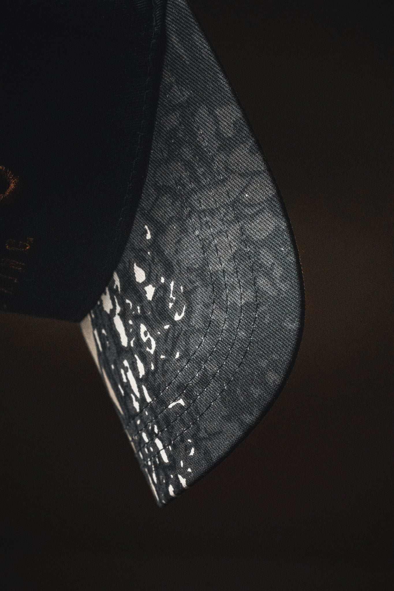A close-up of the “Jesus is King - Black and Darkwood Camo Snapback” by Born United Private Label, a black baseball cap with a curved brim featuring a white speckled camo pattern, designed in the style of an embroidered Christian hat.