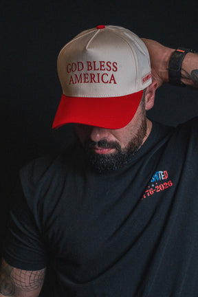 A man faces downward against a dark background, wearing the Born United Private Label God Bless America Snapback in red and white embroidery and a black shirt with the UNITED 1776-2026 logo.