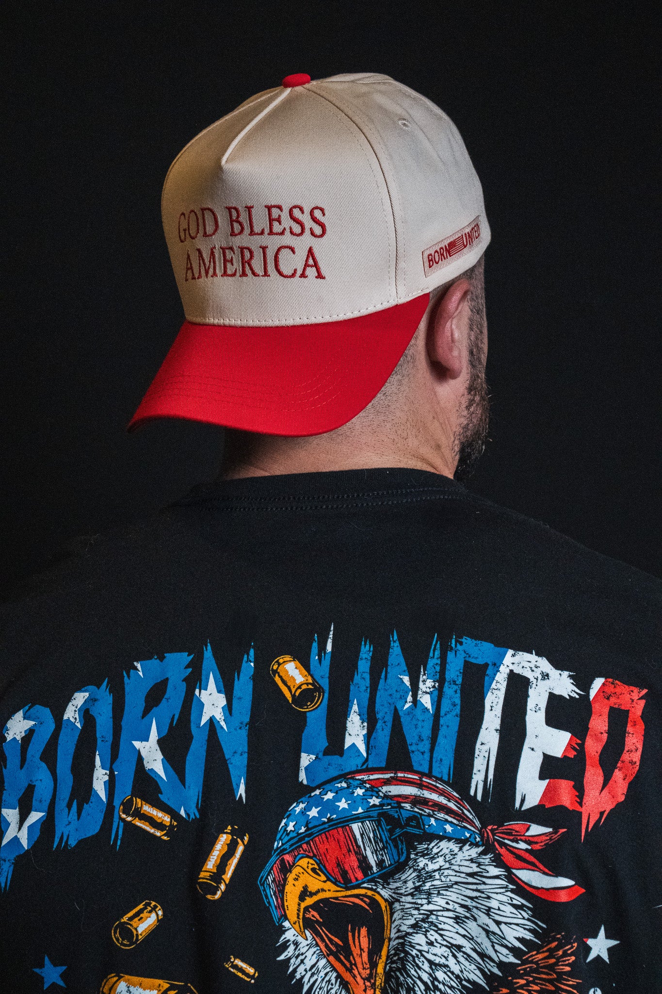 A person shown from behind wearing a Born United Private Label God Bless America Snapback and a Born United shirt featuring an eagle design and bullet graphics.