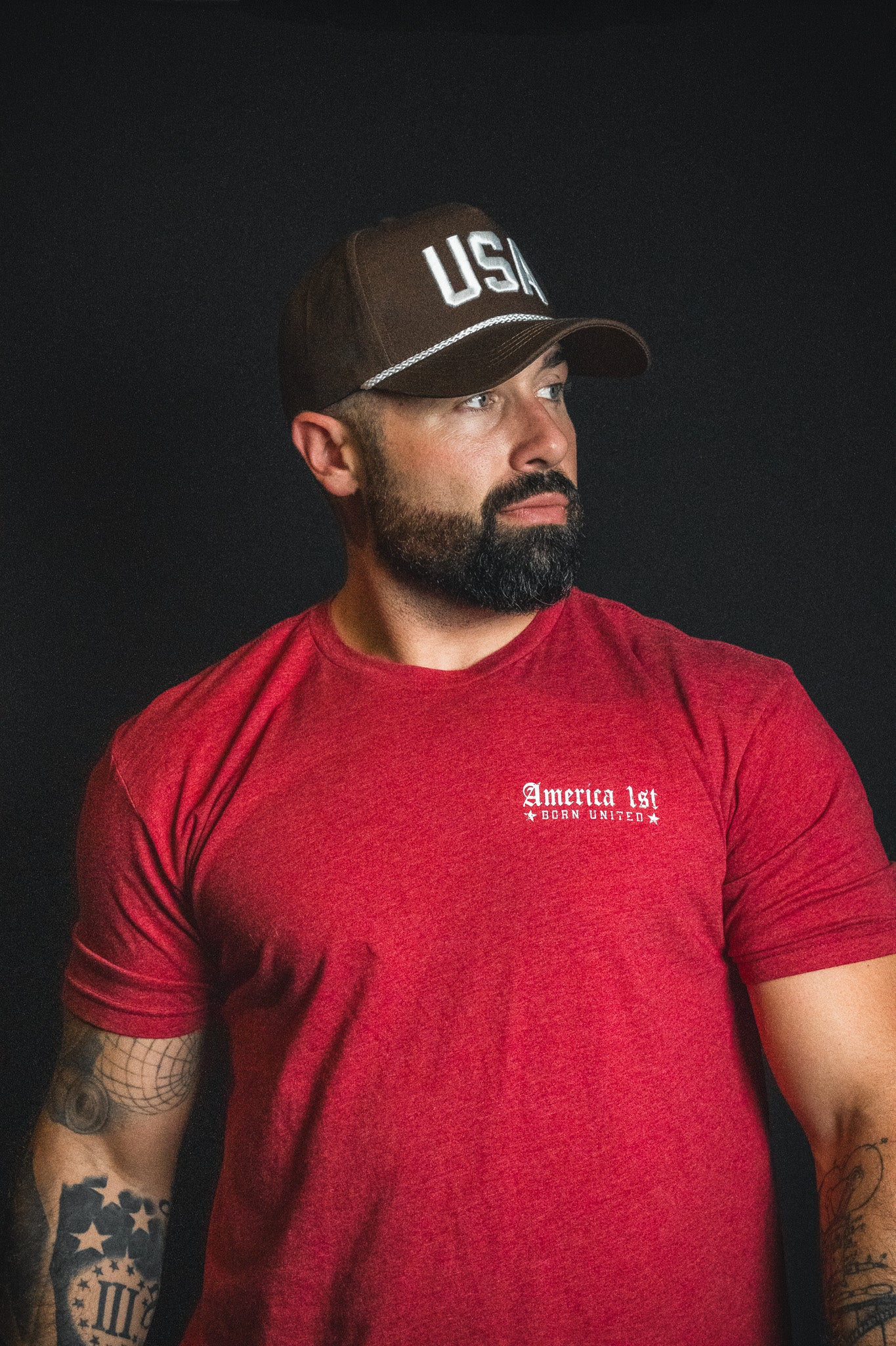 A bearded man in a red t-shirt wears the Born United Private Label USA Brown Snapback Hat, standing against a black background and looking to his left.