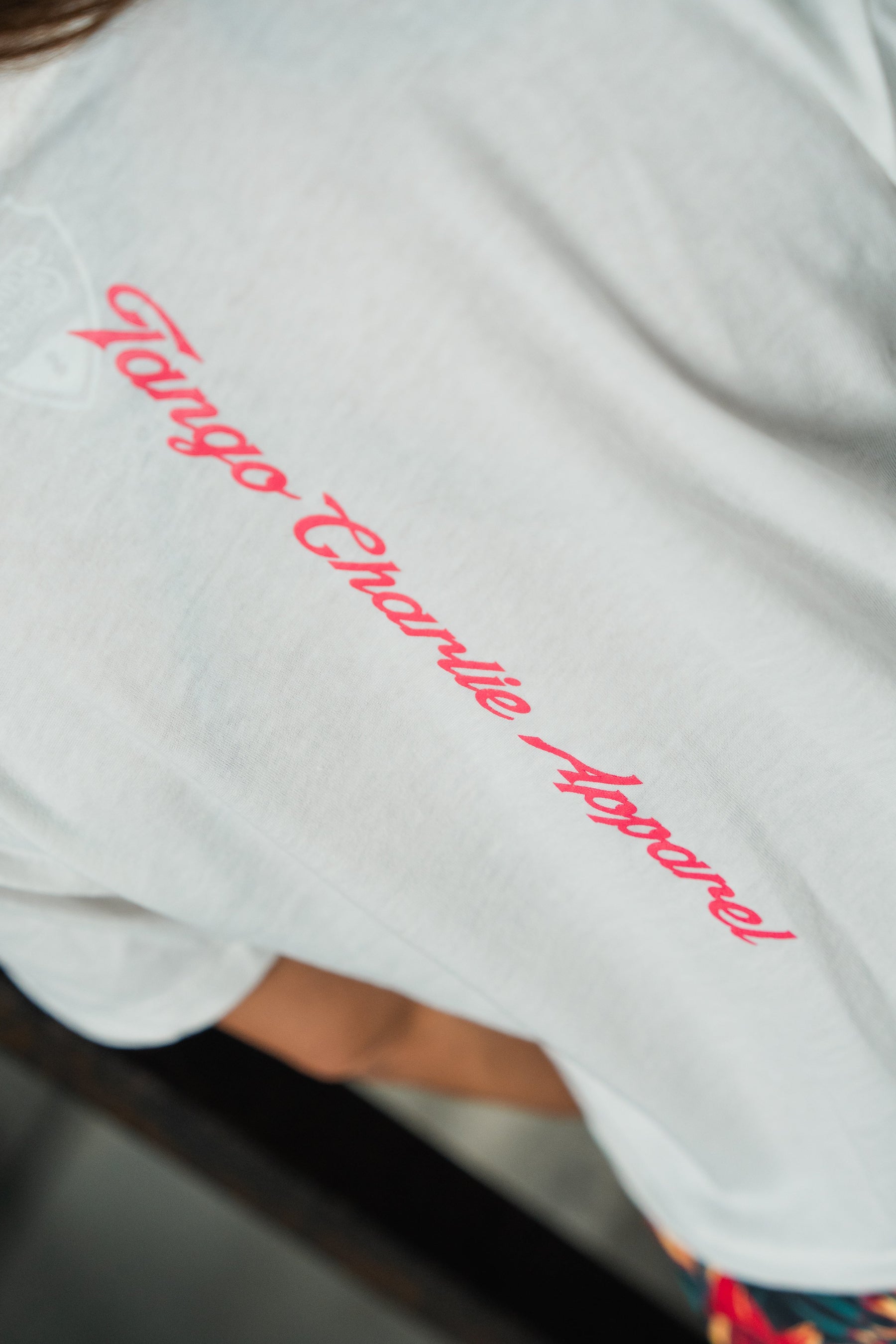 A close-up of the Feral - Women's White Crop by Tango Charlie Apparel, featuring pink cursive Tango Charlie Apparel lettering on the back.