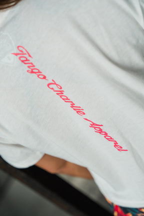 A close-up of the Feral - Women's White Crop by Tango Charlie Apparel, featuring pink cursive Tango Charlie Apparel lettering on the back.