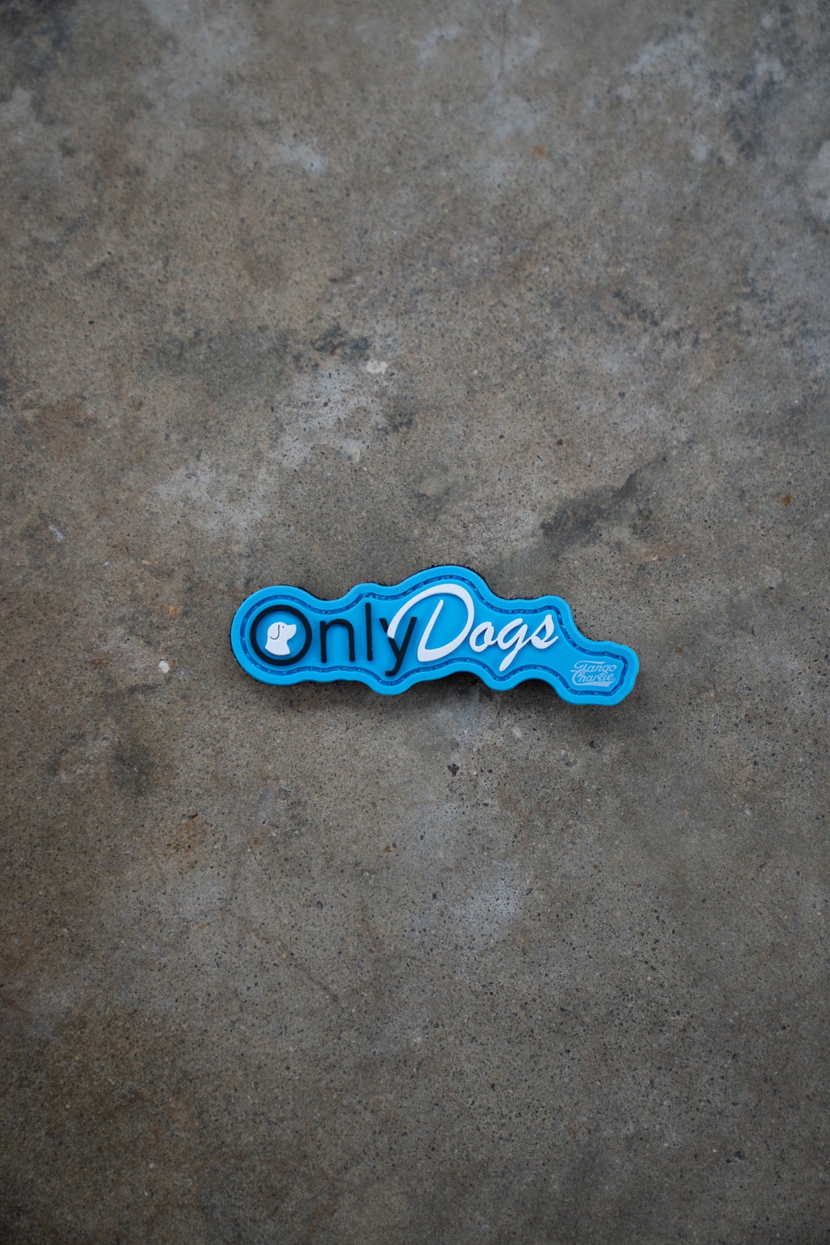 The Only Dogs PVC Patch by Tango Charlie Apparel is shown resting on a textured gray concrete surface.