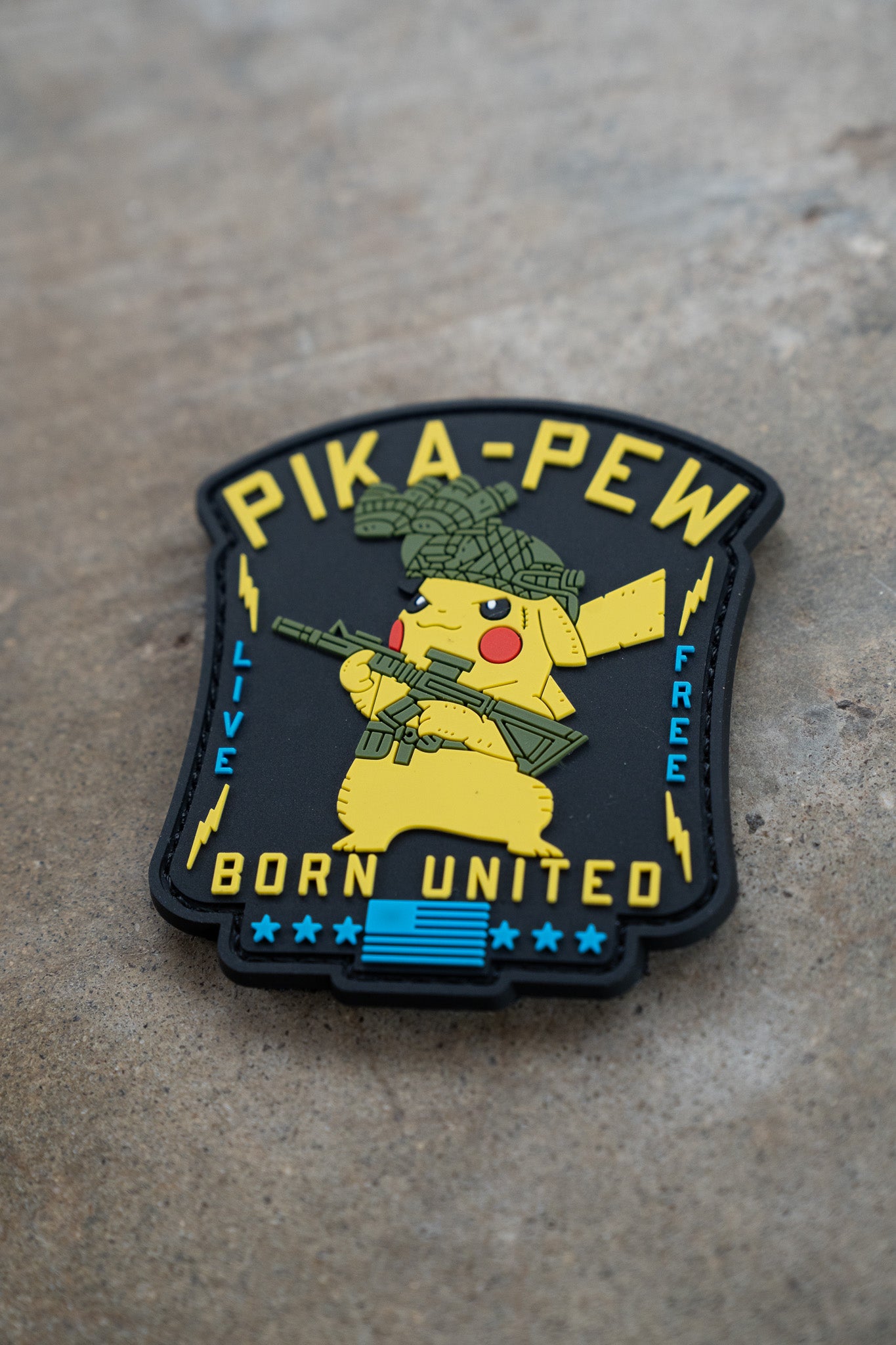 The Pika Pew PVC Patch by Born United Private Label shows Pikachu with a helmet and rifle, plus "PIKA-PEW," "LIVE FREE," and "BORN UNITED" in yellow and blue on black—ideal for Pokemon fans!.