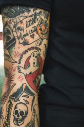Arm covered in Operation Nightmare Tee - Glow in the Dark horror-themed tattoos, including a ghost, a skull, and the text My little food critter.