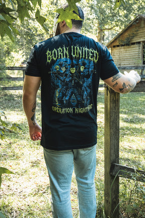 A person wearing a black Operation Nightmare Tee - Glow in the Dark, featuring a graphic of three figures in tactical gear and hockey masks with glow-in-the-dark text.
