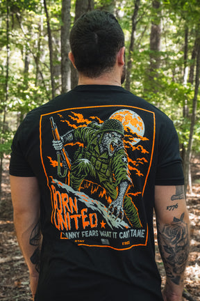 Back view of a person wearing a black Full Moon Tee featuring a tactical werewolf soldier holding a rifle in front of a full moon, with the text BORN UNITED and ANY FEARS WHAT IT CANT TAME.