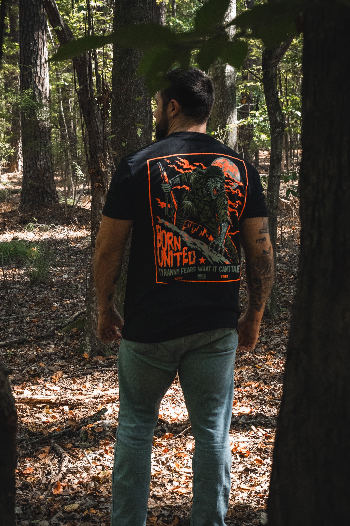 A man wears a black Full Moon Tee featuring a back graphic of a soldier and a full moon with the text, Tyranny fears what it cant tame.