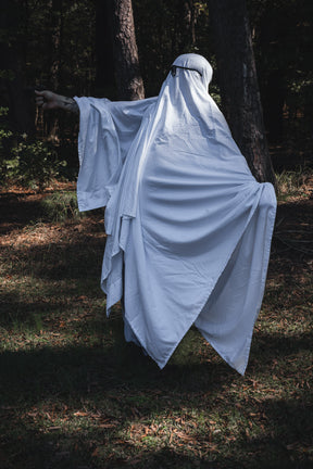 A person wearing a white Ghost Ops Tee sheet ghost costume and glasses points an arm while standing in a forest.