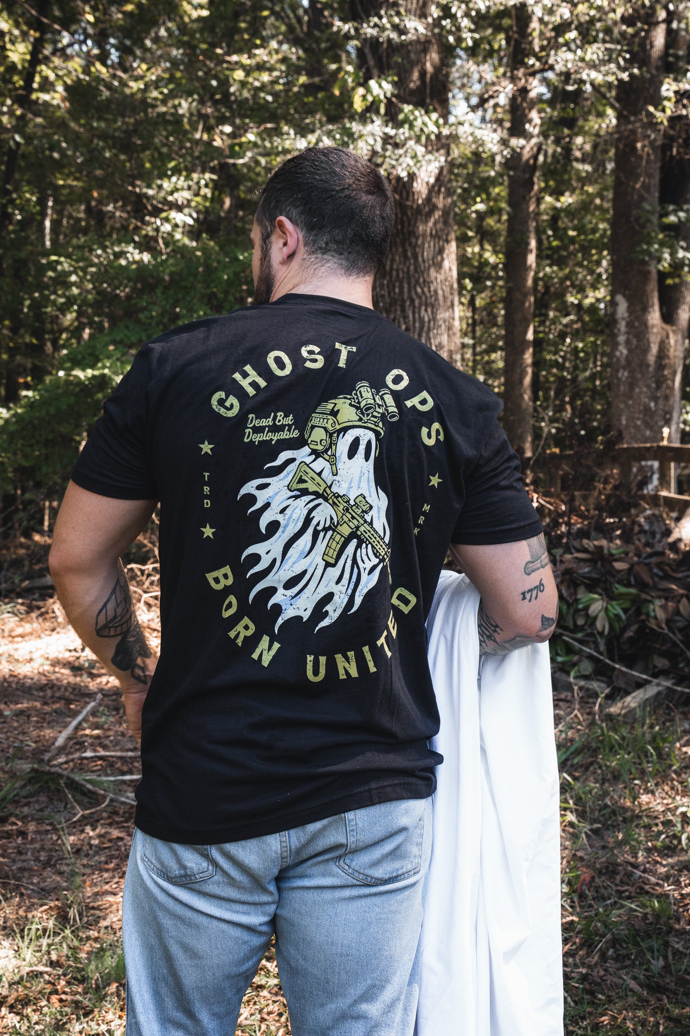 A person seen from the back wearing a black Ghost Ops Tee, featuring a graphic of a ghost in tactical gear holding a rifle with the text Dead But Deployable.
