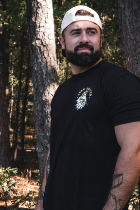A bearded man wears a white baseball cap and a Ghost Ops Tee featuring a graphic of a ghost holding a rifle.