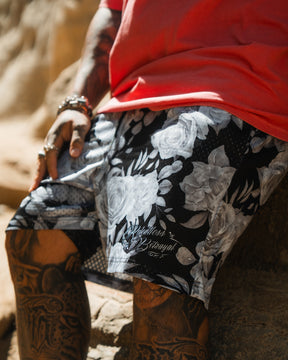 Wearing Relentless Betrayal’s Premium Mesh Shorts | 5- Beauty in Darkness, a person with detailed tattoos and bracelets sits on a rock. Sunlight highlights the textures and patterns of their outfit.