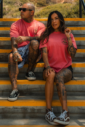 A tattooed man and woman relax on outdoor steps in matching Relentless Betrayal Into the Storm Premium Watermelon T-Shirts, made from quality jersey cotton. The unisex design pairs effortlessly with shorts and sneakers for a confident look.