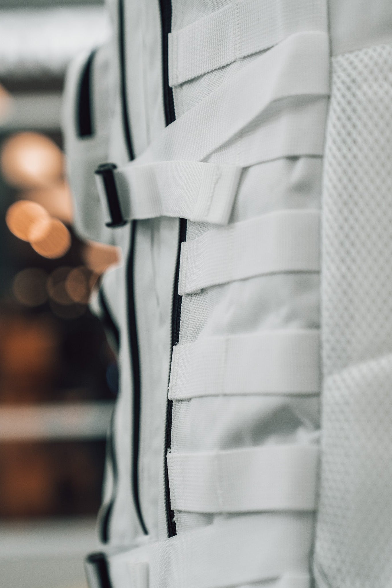 Close-up of the Born United Private Label Storm Trooper Tac-Pac - 45L, a white fabric bag with horizontal straps and mesh texture, inspired by Star Wars, set against a blurred background with warm lights.