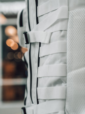 Close-up of the Born United Private Label Storm Trooper Tac-Pac - 45L, a white fabric bag with horizontal straps and mesh texture, inspired by Star Wars, set against a blurred background with warm lights.