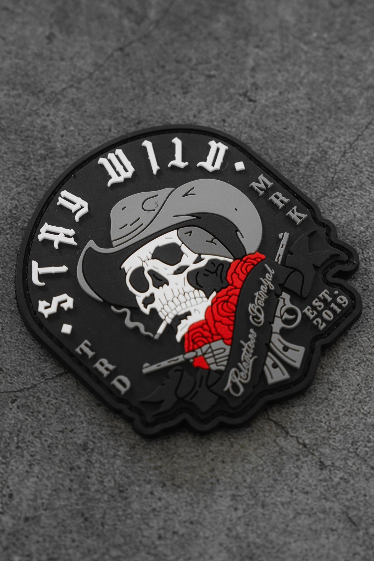 The Stay Wild Patch by Relentless Betrayal is a 3D PVC design with a skull in a cowboy hat, cigarette, red roses, and the text WILD MARKS ERA and EST. 2019 on a textured gray background.
