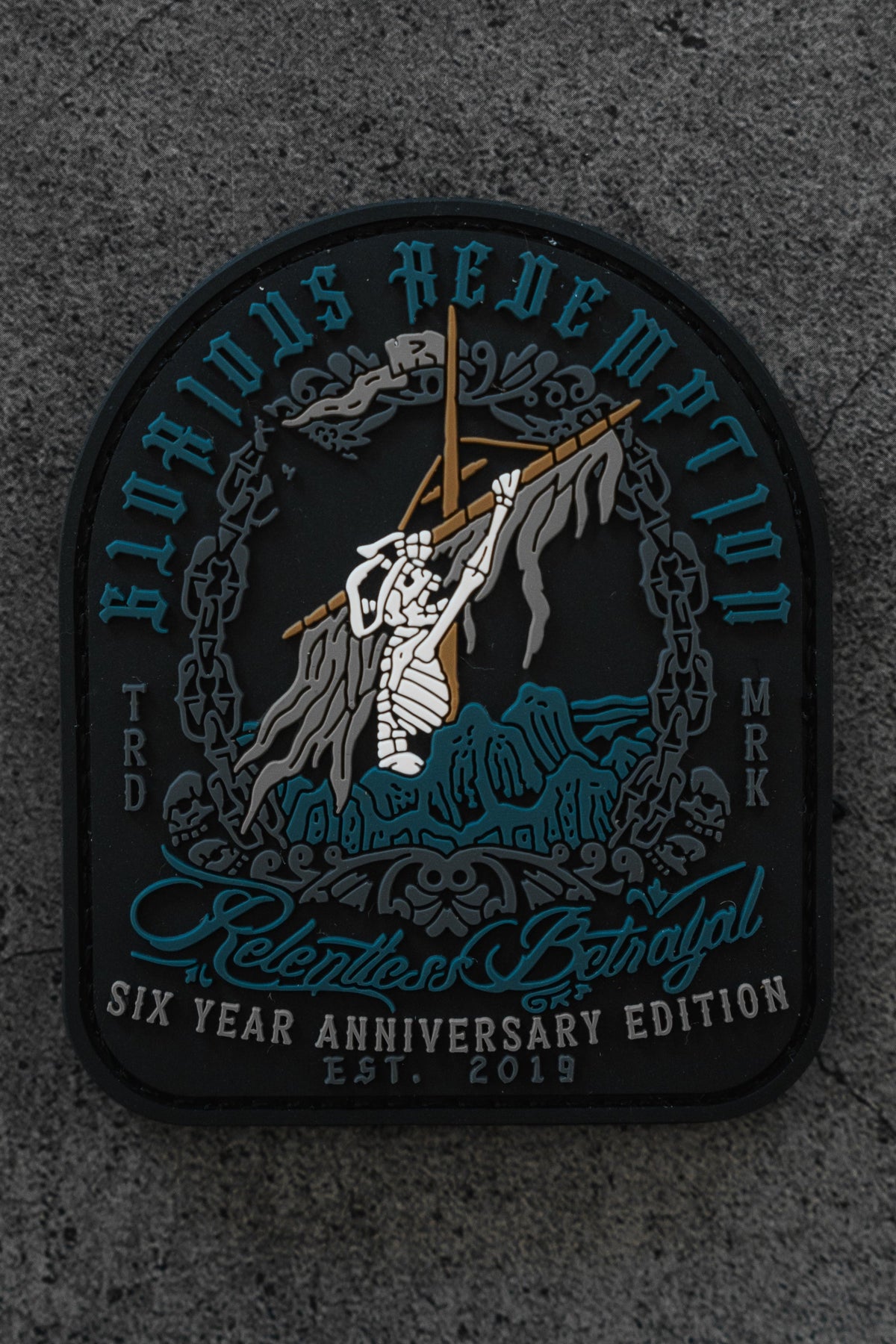 The Glorious Redemption Patch by Relentless Betrayal is a 3D PVC patch showing a skeleton climbing a rocky hill with a cross, surrounded by blue and white text: Glorious Redemption, Relentless Betrayal, and Six Year Anniversary Edition Est. 2019.