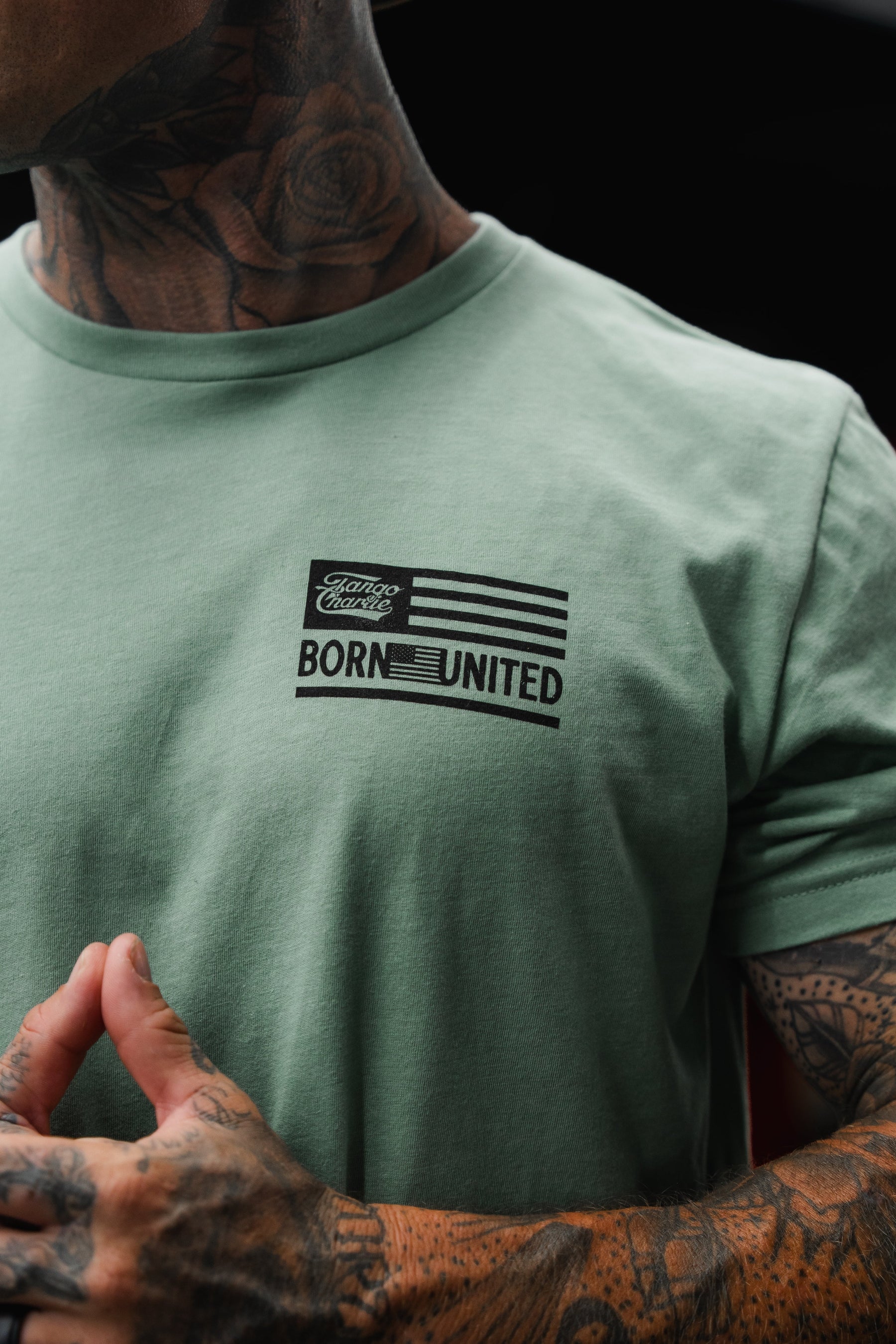 Wearing the Loaded Leopard LHSG - Seafoam Green Tee from Tango Charlie Apparel, a tattooed individual sports a shirt featuring a flag graphic and the bold statement "Tattoo Classic Born United" on the front—channeling serious high-intensity fitness energy alongside the standout motto, "Lift Heavy Shoot Guns.