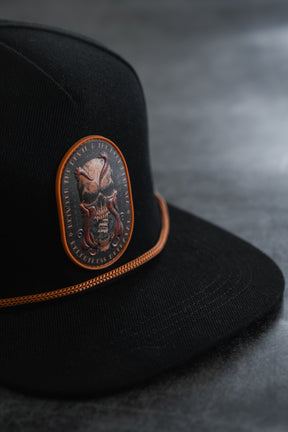 Between The Devil & Deep Blue Sea Snapback by Relentless Betrayal—a black cap featuring an orange-trimmed patch with a fierce skull and tentacles, set against a dark, textured background; this bold nautical snapback makes a striking statement in pirate-inspired style.