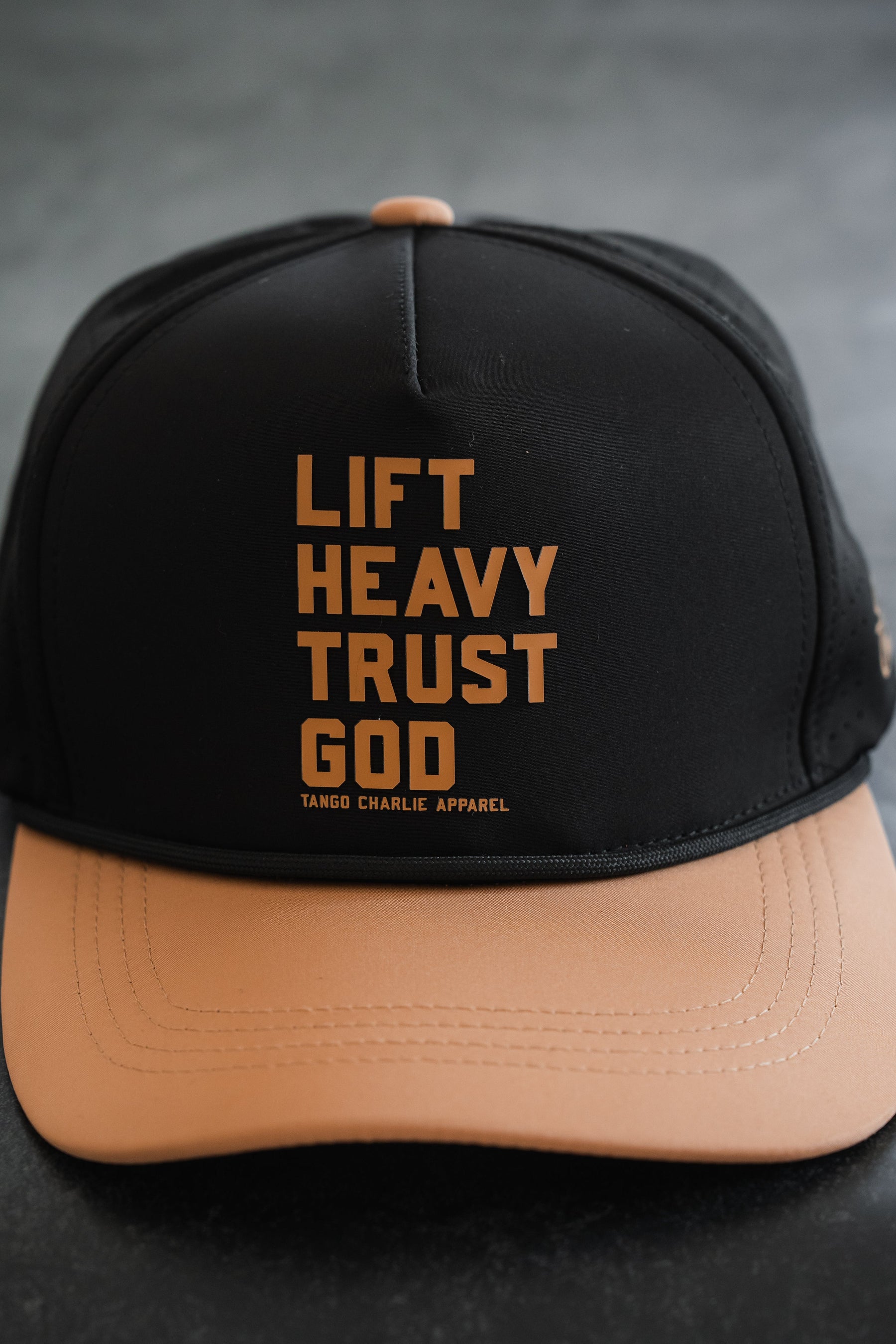 Introducing the Lift Heavy. Trust God. Hydro - Black Snapback Hat from Tango Charlie Apparel, a sweat-resistant Christian gym hat with “Lift Heavy. Trust God.” and the Tango Charlie Apparel logo printed on the front—perfect for workouts and expressing your faith.