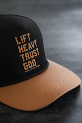 Introducing the Lift Heavy. Trust God. Hydro - Black Snapback Hat by Tango Charlie Apparel—a black and tan, sweat-resistant snapback cap featuring “LIFT HEAVY. TRUST GOD.” and the Tango Charlie Apparel branding on the front panel. This Christian gym hat is perfect for supporting your active lifestyle.
