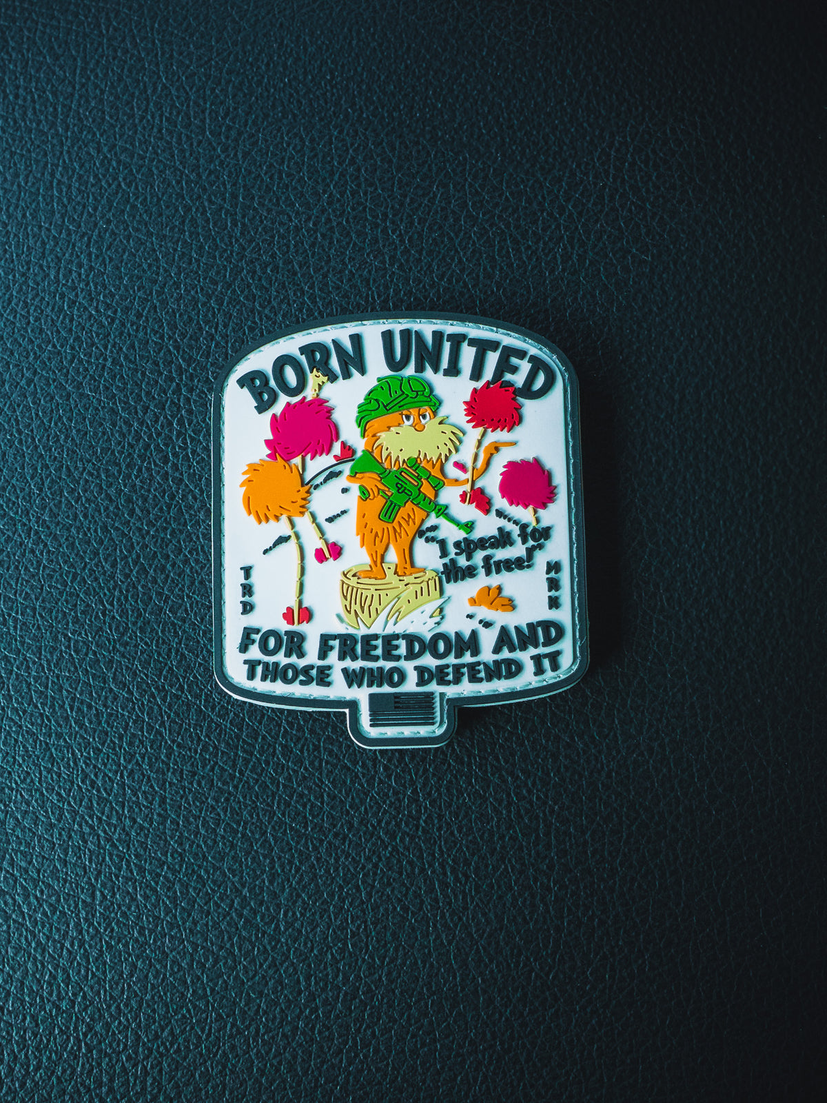 The Speak for the Free PVC Patch by Born United Private Label features a whimsical character and trees with BORN UNITED FOR FREEDOM AND THOSE WHO DEFEND IT on a dark textured background. Velcro backing makes it ideal for tactical gear.