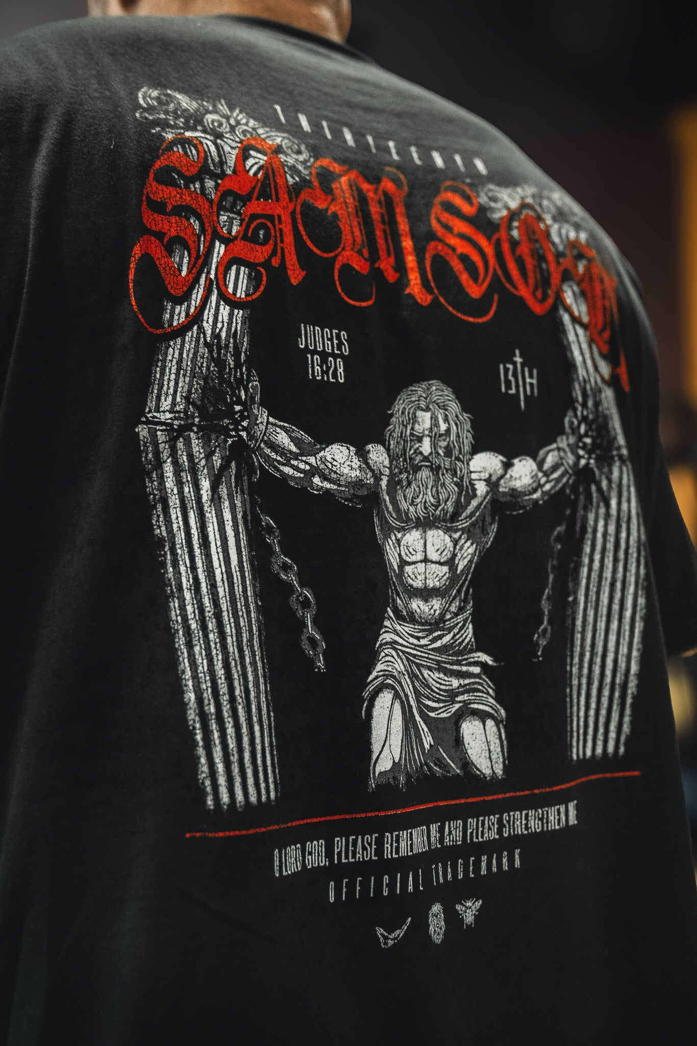 The 13th Samson Premium Tee is a bold, faith-inspired shirt showing muscular Samson breaking pillars, “SAMSON” in red above, and Judges 16:28 below—crafted with premium quality and detailed text and graphics.