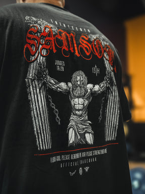 The 13th Samson Premium Tee is a bold, faith-inspired shirt showing muscular Samson breaking pillars, “SAMSON” in red above, and Judges 16:28 below—crafted with premium quality and detailed text and graphics.