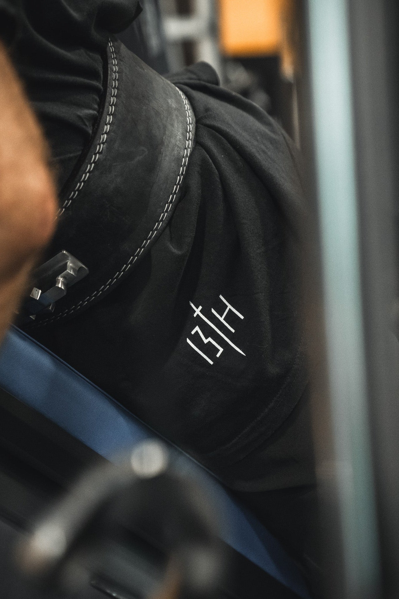 Close-up of a person in black 13th shorts and a weightlifting belt, wearing the Samson Premium Tee by 13th—faith-inspired athletic apparel—seated on gym equipment, preparing to lift.