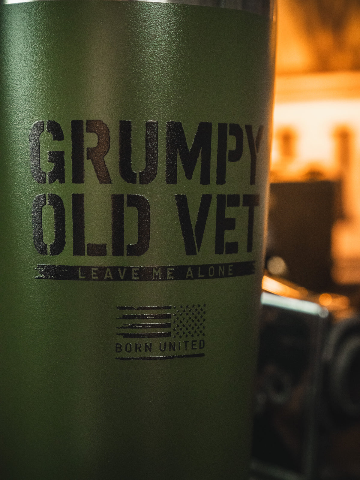 The Grumpy Old Vet Tumbler - 20oz by Born United Private Label is a green stainless steel tumbler with black "GRUMPY OLD VET - LEAVE ME ALONE" text, a small American flag, and "BORN UNITED." It keeps drinks hot or cold on the go.