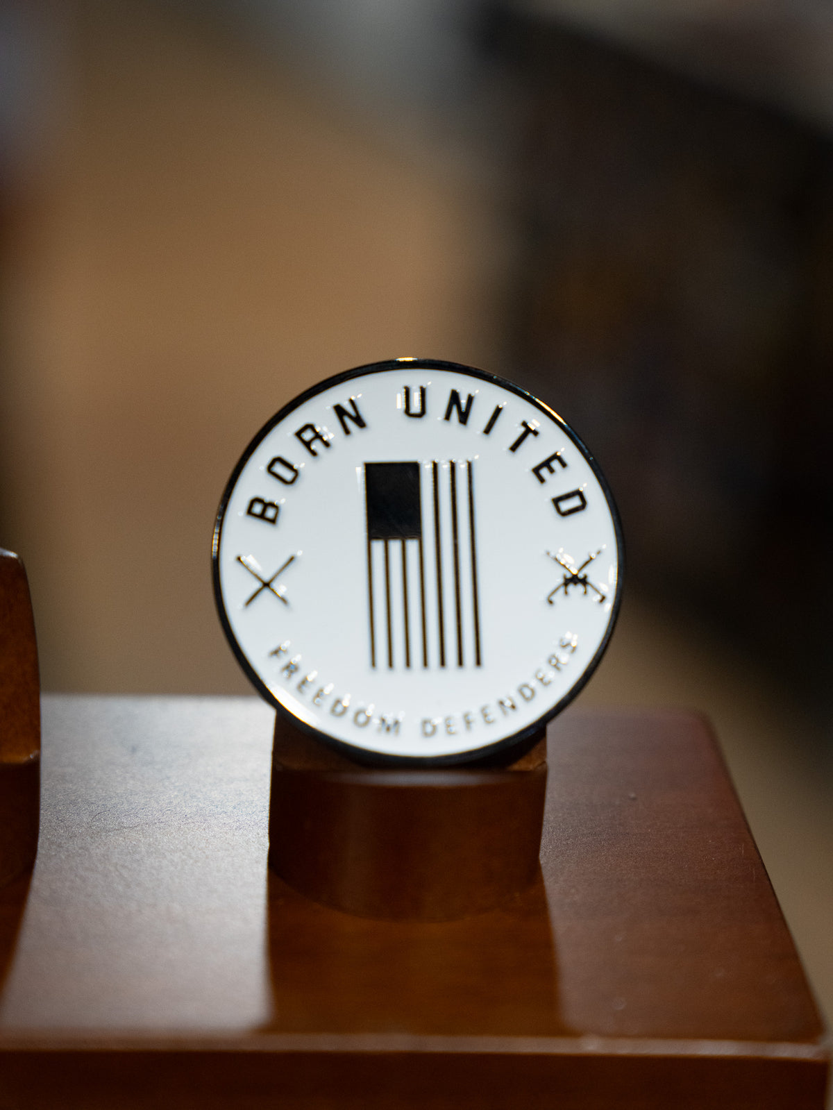 The Speak for the Free! Challenge Coin from Born United features a black-and-white American flag, crossed swords, “BORN UNITED” above, “FREEDOM DEFENDERS” below, and “Speak for the Free” on a wooden stand.