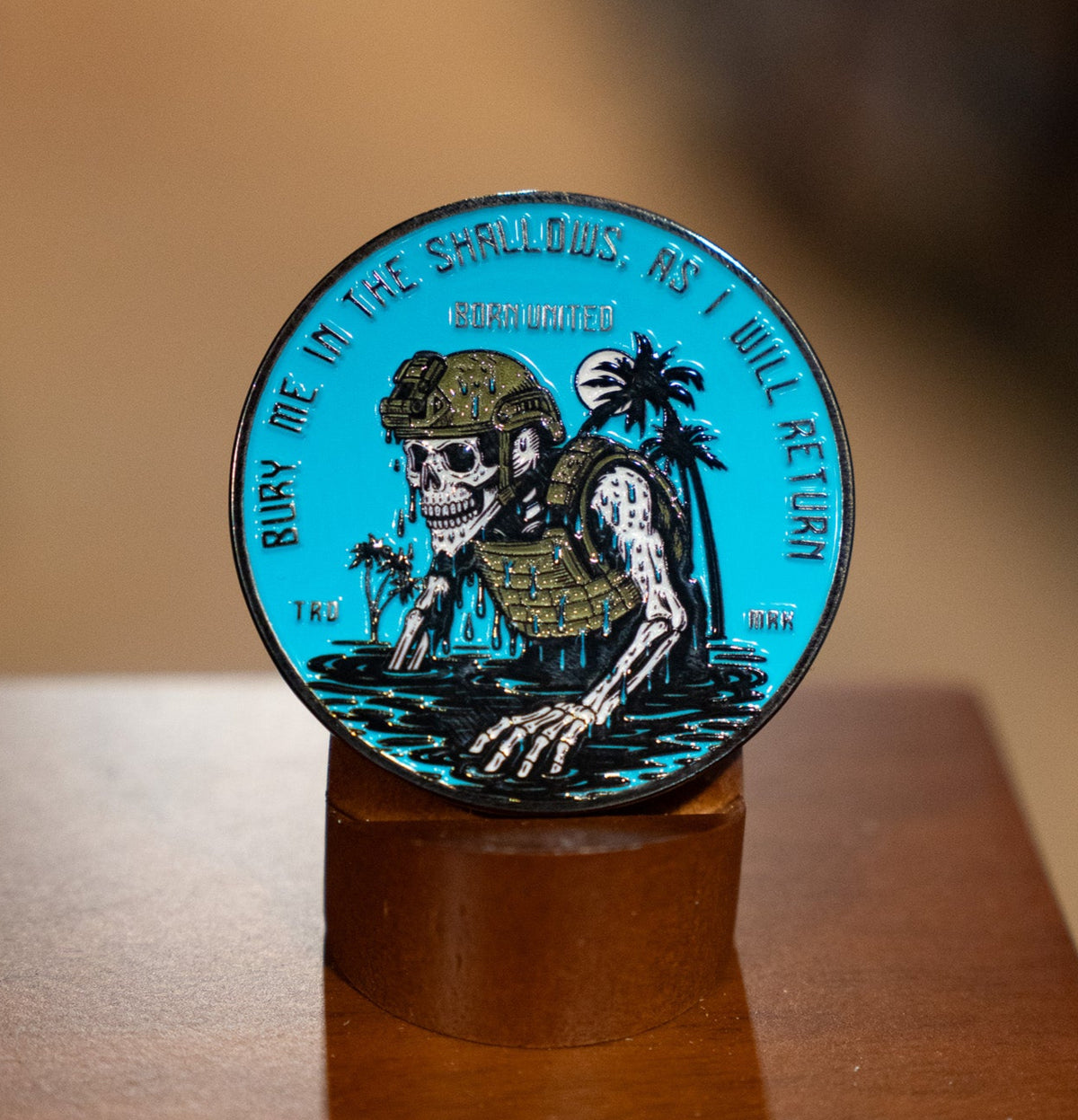 The Shallows Challenge Coin by Born United Private Label shows a skeleton in military gear rising from water with palm trees, encircled by the words, "Bury me in the shallows, as I will return.