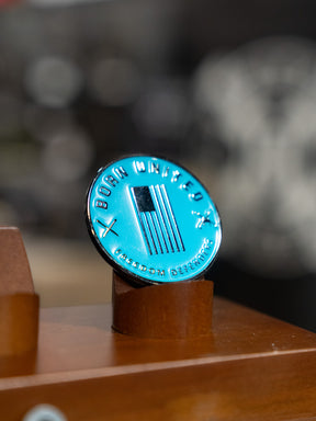 The Born United Private Label Shallows Challenge Coin features an American flag, crossed swords, and “Born United” and “Freedom Defender,” standing upright on a wooden stand—a reminder to never ask, "Bury me in the shallows.