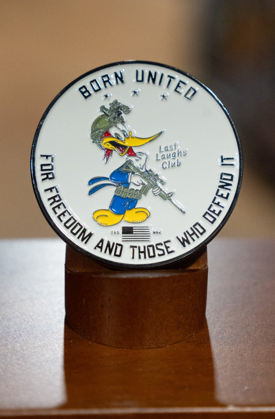 The Last Laughs Club Challenge Coin by Born United Private Label features a cartoon duck in military gear with a rifle, the phrase "BORN UNITED FOR FREEDOM AND THOSE WHO DEFEND IT," and Last Laughs Club proudly displayed at the center.