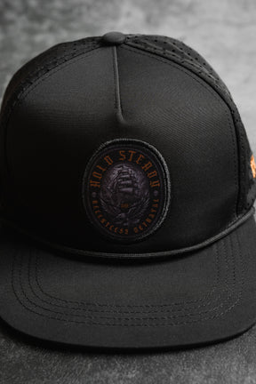 A close-up of the Hold Steady Ghost Snapback by Relentless Betrayal—a premium snapback baseball cap with a round patch reading HOLD STEADY BREATHLESS BETRAYED in orange and showcasing a coiled snake.