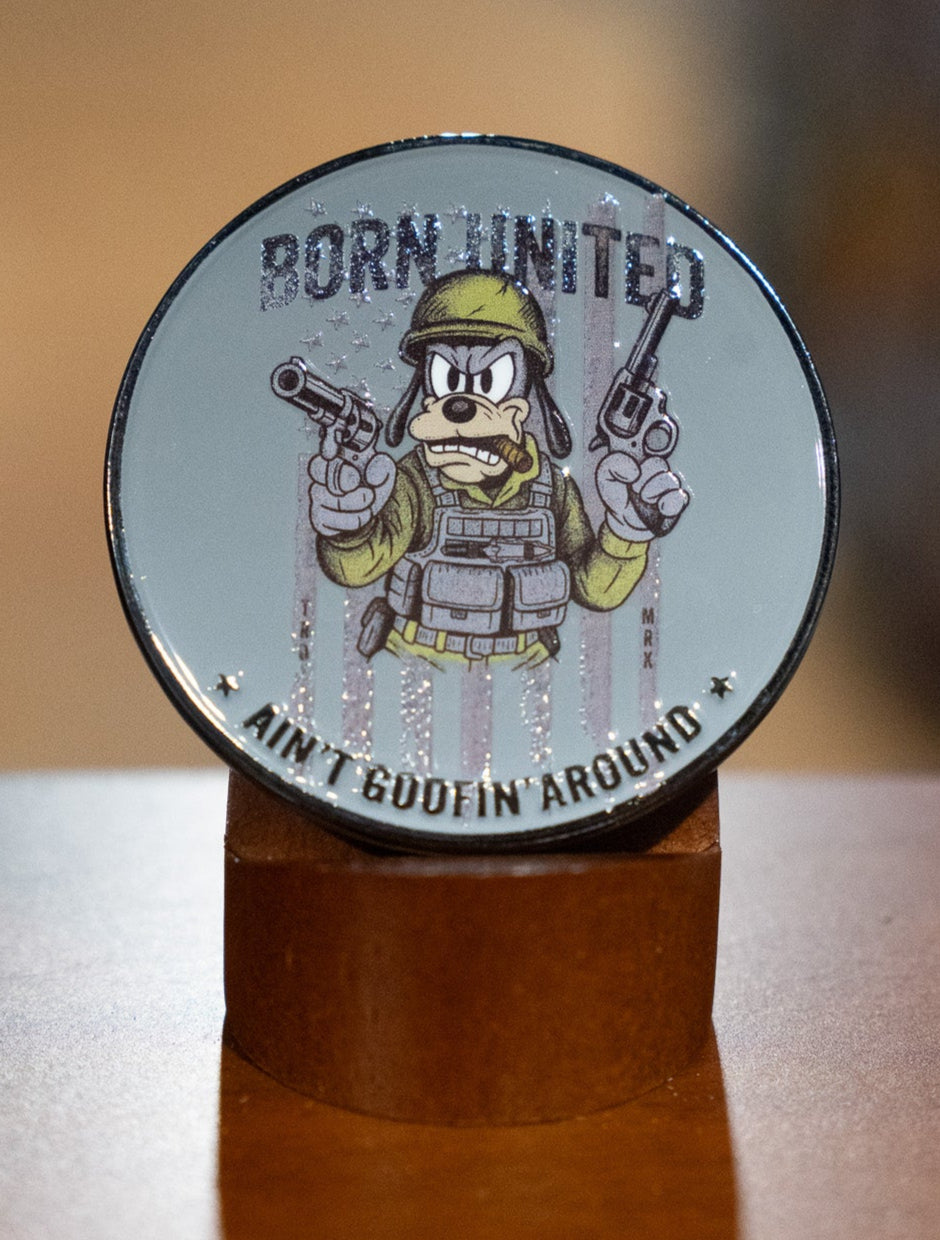 The Ain't Goofin' Around Challenge Coin by Born United Private Label features a cartoon dog in military gear with two pistols, "BORN UNITED" above, and "Ain't Goofin Around" below. Perfect for collectors, it comes on a brown display stand.