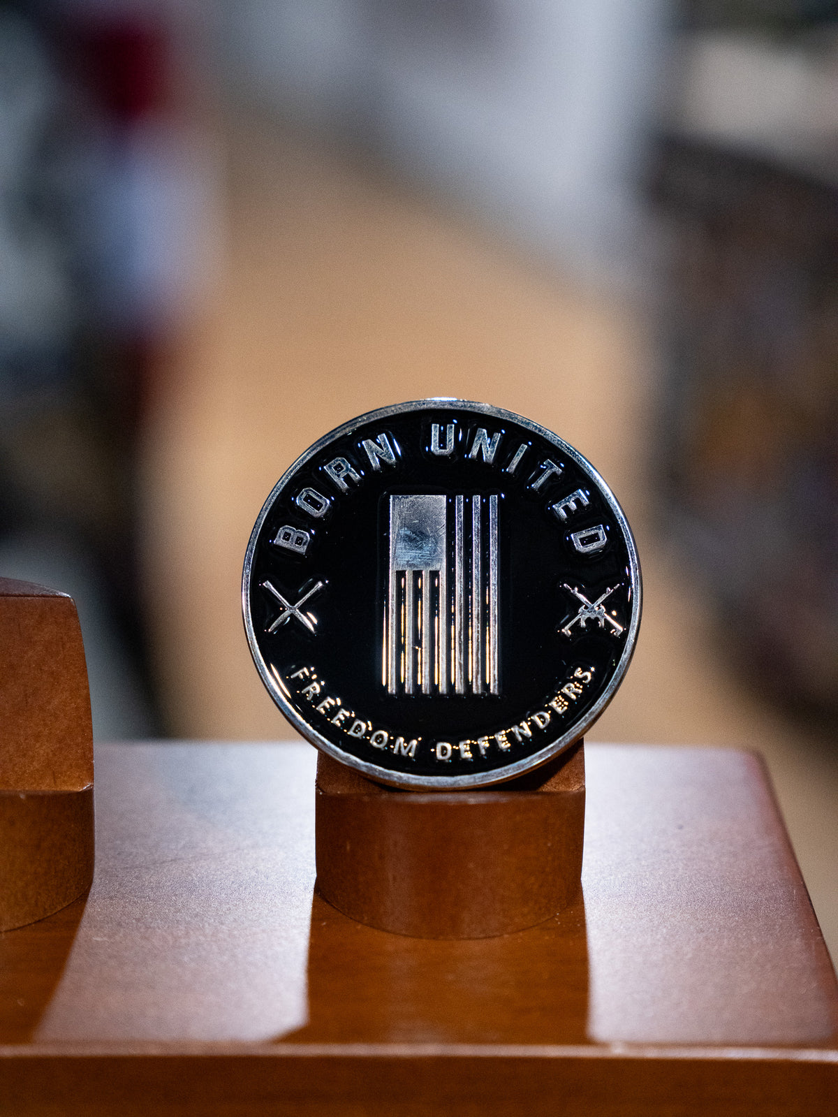 The Legend - Balboa Challenge Coin by Born United Private Label features a stylized American flag, crossed rifles, and “BORN UNITED” with “FREEDOM DEFENDERS,” displayed upright on a wooden stand—a standout commemorative piece.