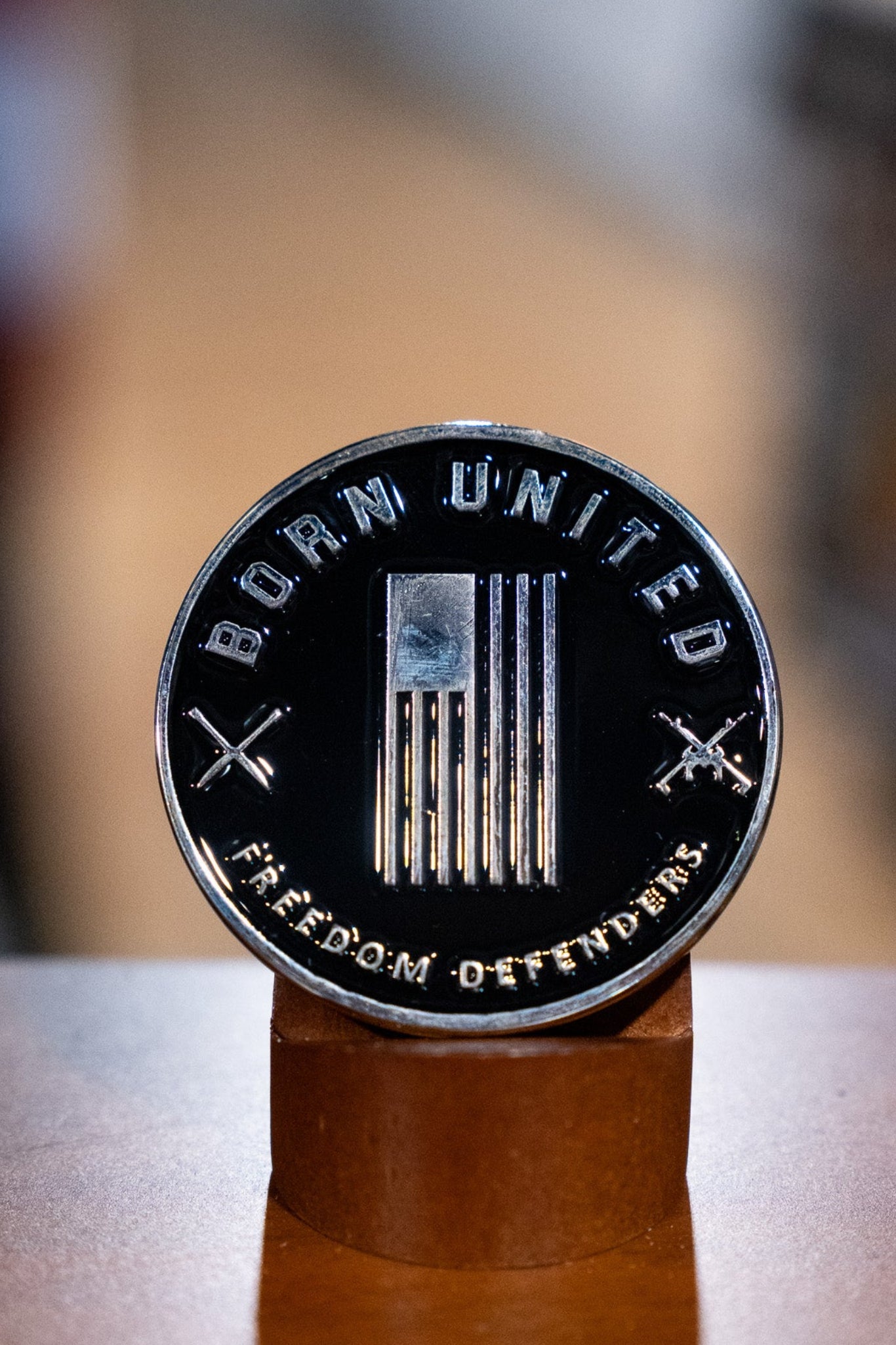 The Legend - Balboa Challenge Coin by Born United Private Label features a stylized American flag, crossed rifles, and “BORN UNITED” with “FREEDOM DEFENDERS,” displayed upright on a wooden stand—a standout commemorative piece.
