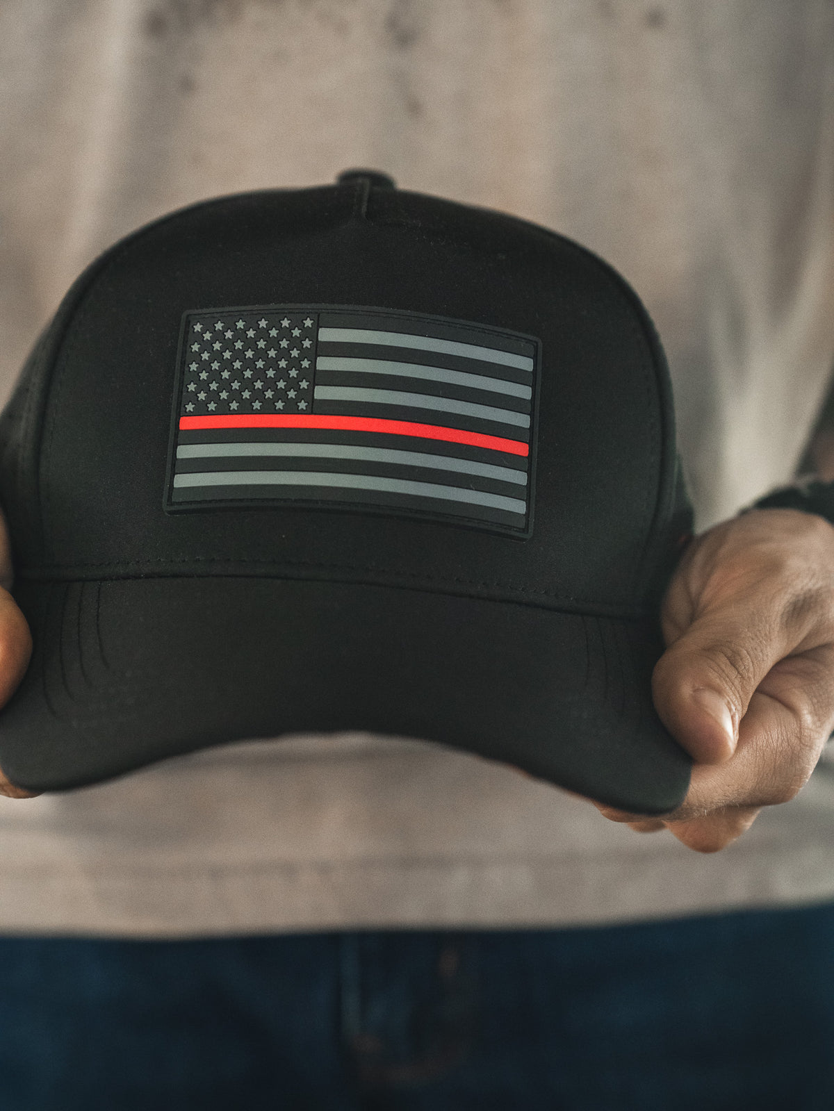 Someone holds the Born United Premium Flag Snapback - TRL by Born United Private Label—a black cap with a grayscale American flag and a single red stripe, symbolizing firefighter support.