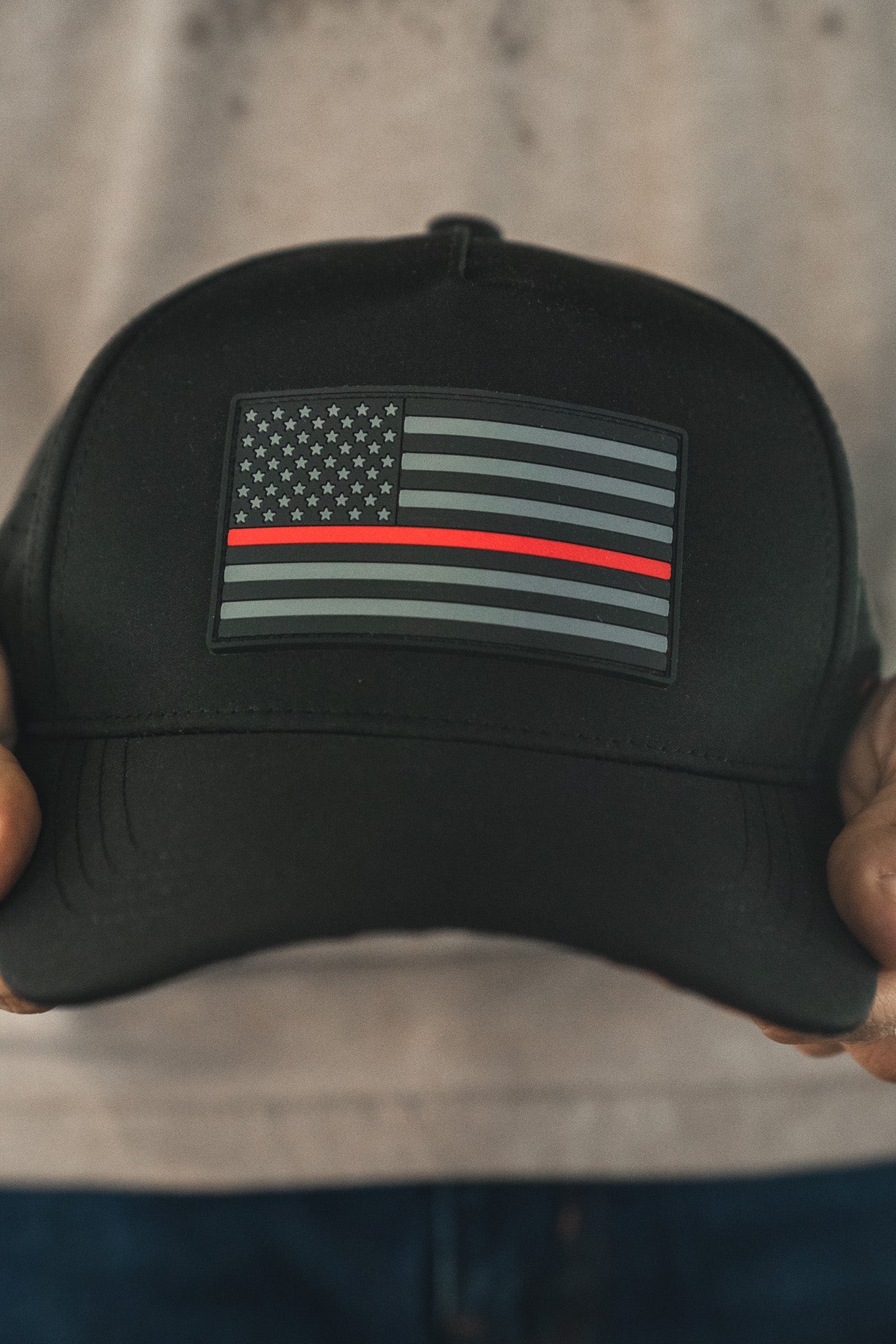 Someone holds the Born United Premium Flag Snapback - TRL by Born United Private Label—a black cap with a grayscale American flag and a single red stripe, symbolizing firefighter support.