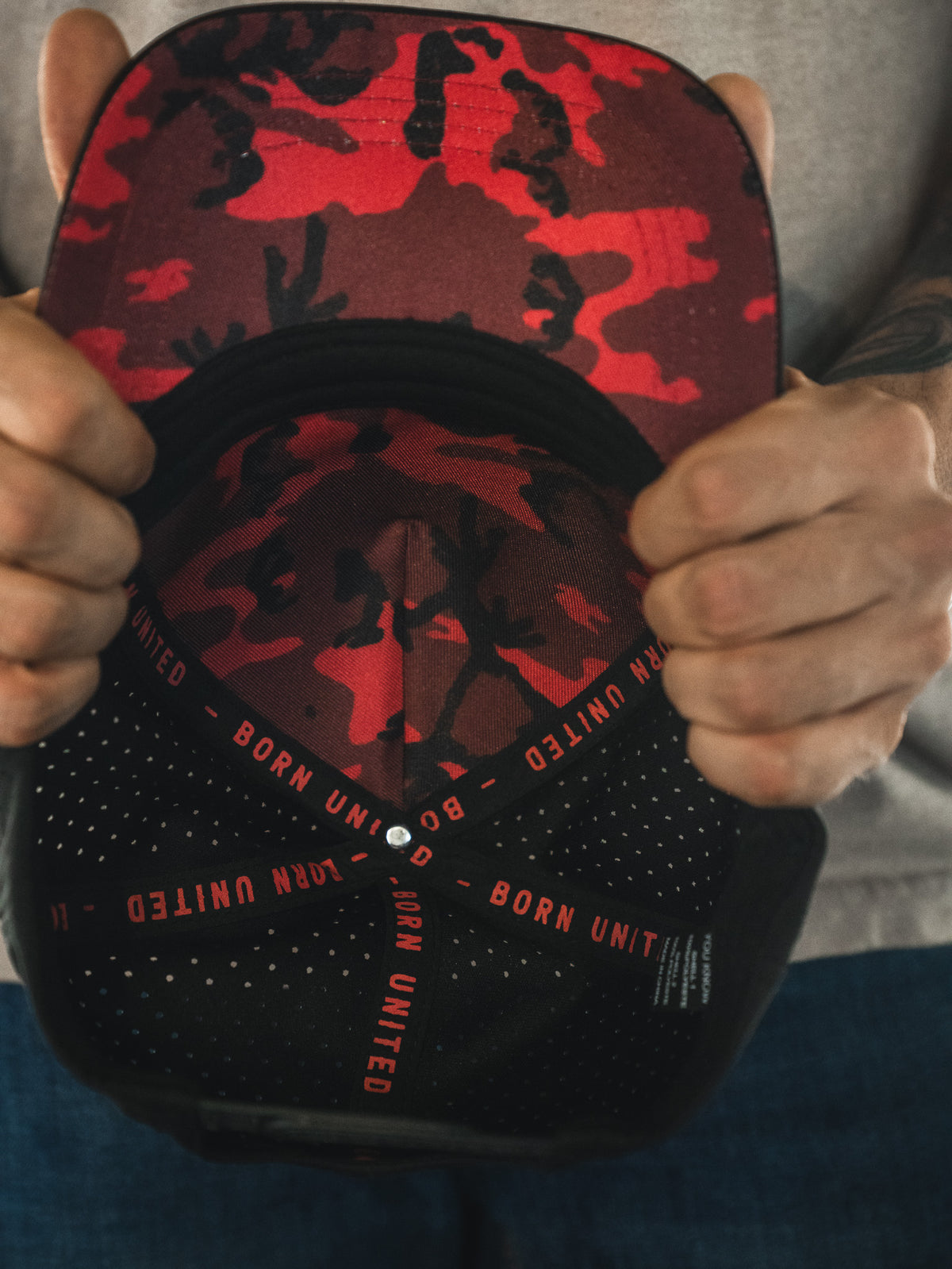 A person holds the Born United Premium Flag Snapback - TRL from Born United Private Label, displaying its interior with black fabric strips repeatedly featuring "BORN UNITED.