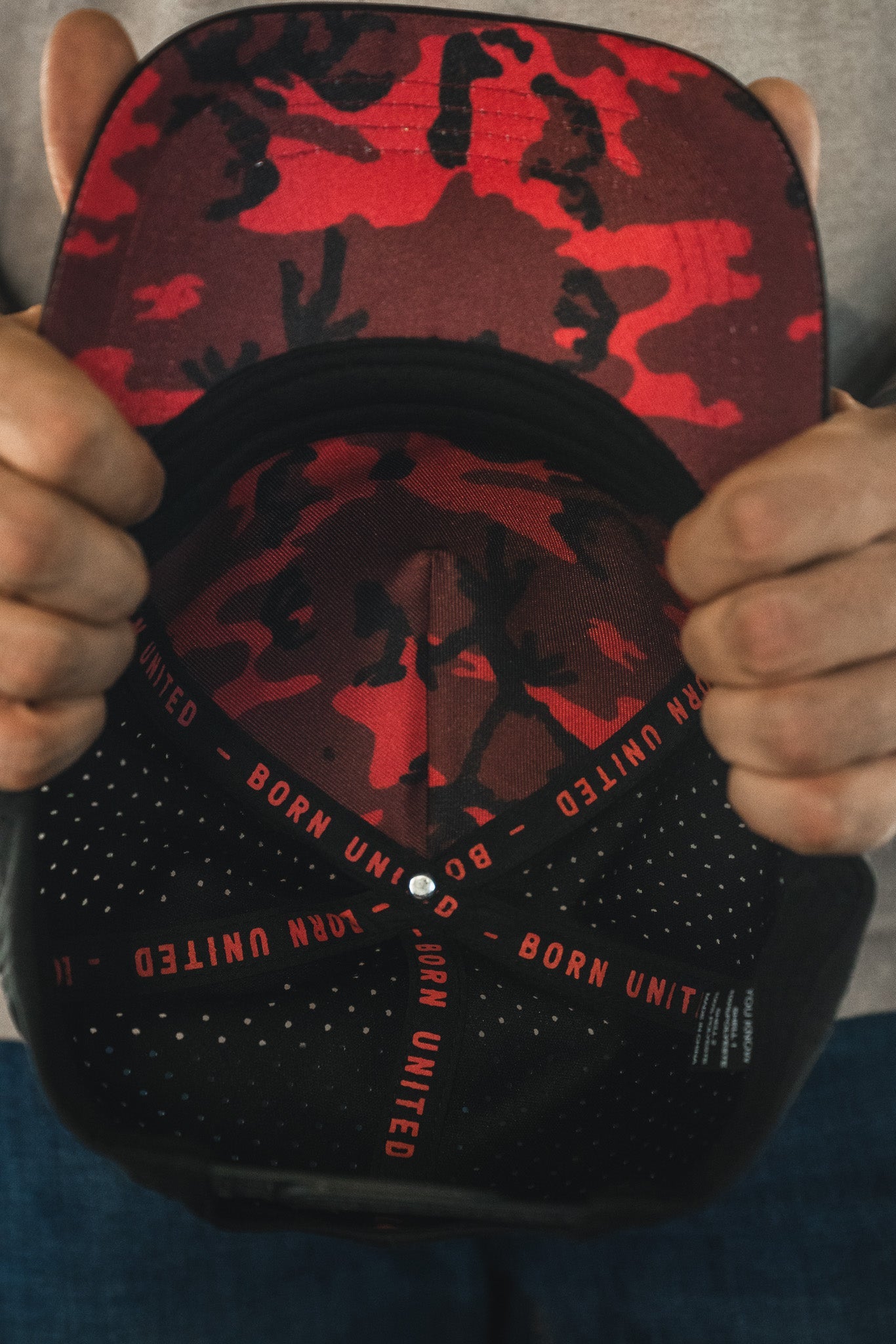 A person holds the Born United Premium Flag Snapback - TRL from Born United Private Label, displaying its interior with black fabric strips repeatedly featuring "BORN UNITED.