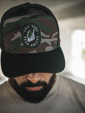 A bearded man looks down, wearing the Born United Premium Snapback - Full Send (Camo) by Born United Private Label. Only the upper part of his face is visible, with a softly blurred background.
