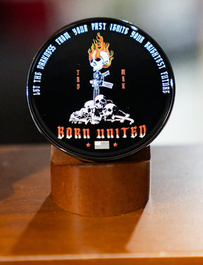 The Let the Darkness Challenge Coin by Born United Private Label features a round black tin with a flaming skull, crossed rifles, and central skulls. The tin reads “LET THE DARKNESS FROM YOUR PAST IGNITE YOUR BRIGHTEST FUTURE” and “BORN UNITED,” plus an American flag.