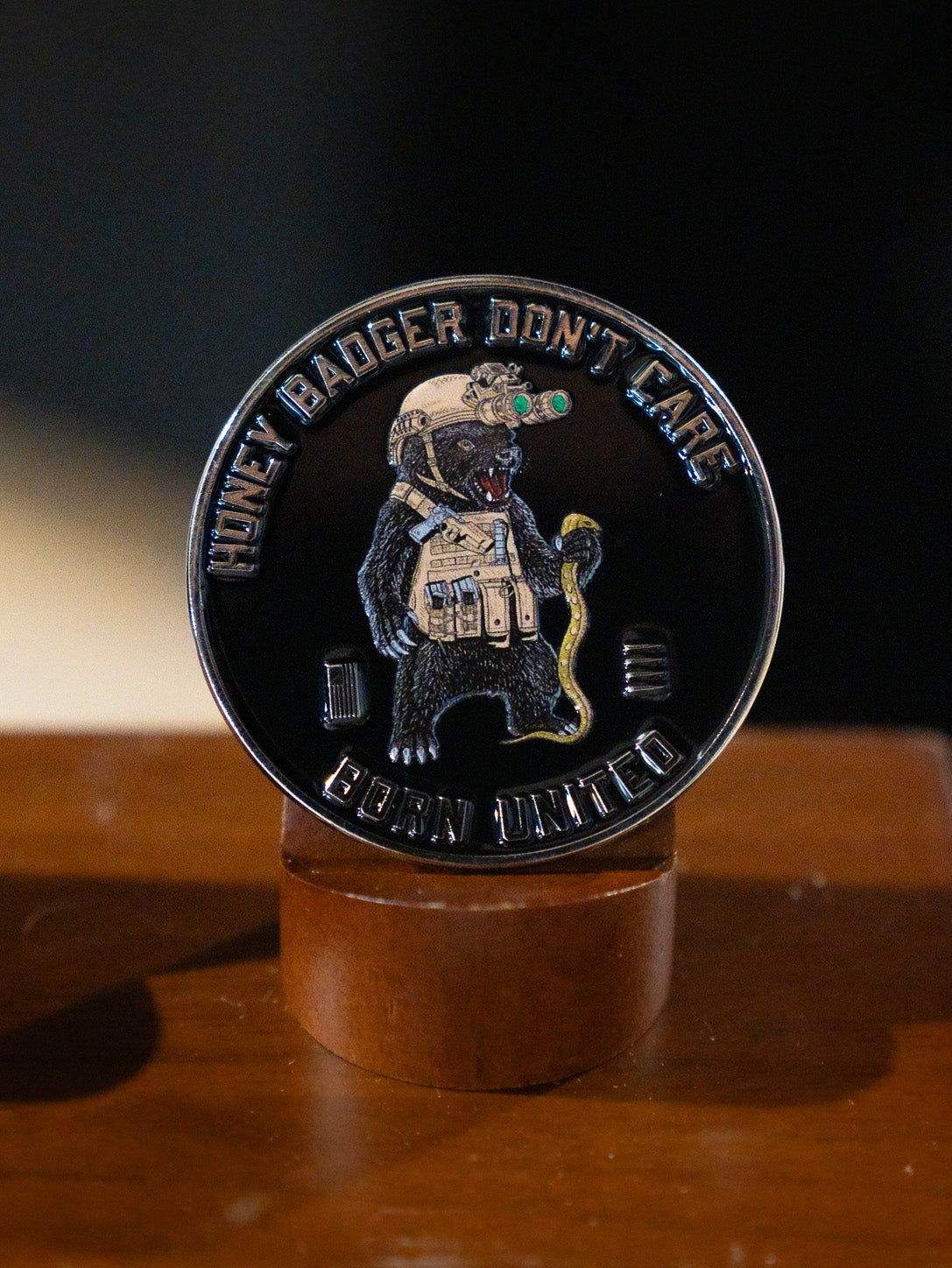 The Honey Badgerin' Challenge Coin by Born United Private Label features an armored honey badger with a snake and night-vision goggles, plus "HONEY BADGER DONT CARE" and "CUBAN UNITED" text around the edge, shown on a wooden stand.